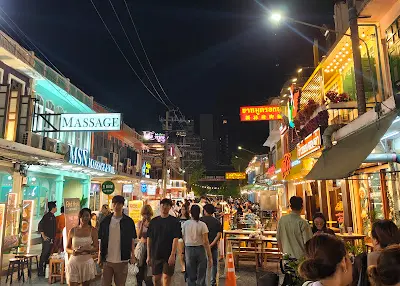 A bustling street food market at night in Bangkok, Thailand, a cheap international travel hub.